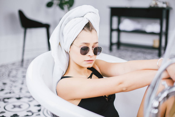 Giovane donna caucasica con asciugamano sulla testa e occhiali da sole ottenere un trattamento termale in un salone di bellezza, all'interno di una stanza interna. Rilassarsi in bagno in biancheria. Il concetto di cura del corpo e relax
 - Foto, immagini
