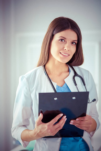 Female doctor standing with a folder in her hands at hospital, smiling at the camera - Foto, Imagen