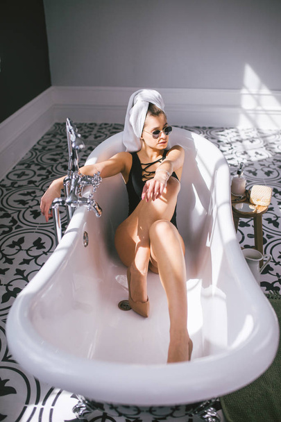 Mulher caucasiana jovem com toalha na cabeça e óculos de sol recebendo tratamento de spa em um salão de beleza, dentro de uma sala interior. Relaxar na casa de banho de linho. O conceito de cuidado corporal e relaxamento
 - Foto, Imagem