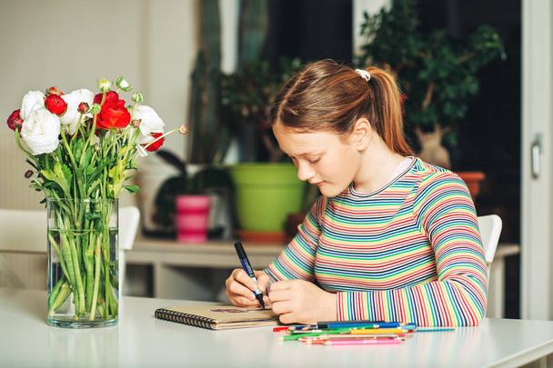 Молода дівчина-підліток малює вдома, сидячи за столом
 - Фото, зображення