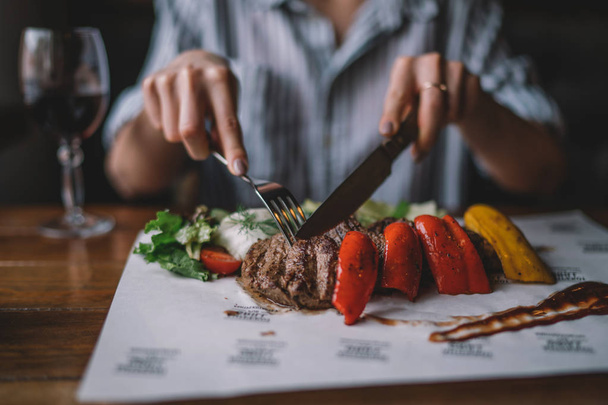 Spicy grilled lamb leg with vegetables and herbs on a roasting cast iron. Barbecue lamb with vegetables. Healthy food. Eating and leisure concept. Woman having dinner at table with food. Toned image. - Foto, Imagem