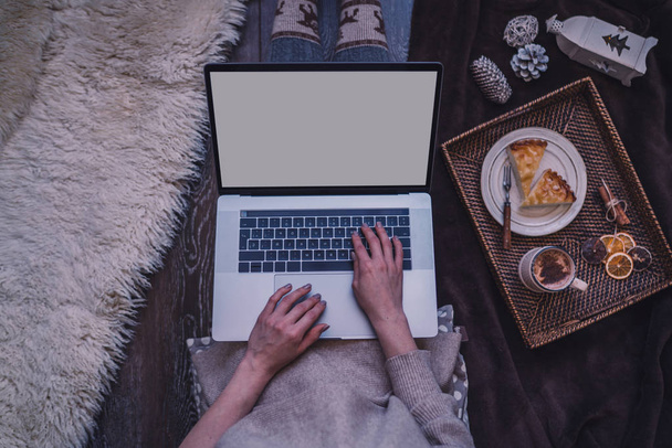 Christmas online shopping. Woman buys presents, prepare to xmas eve. Female with laptop, copy space on screen. Hot coffee, spice and almond cakes on tray. Cozy blanket. Toned image. Soft focus. - Photo, image