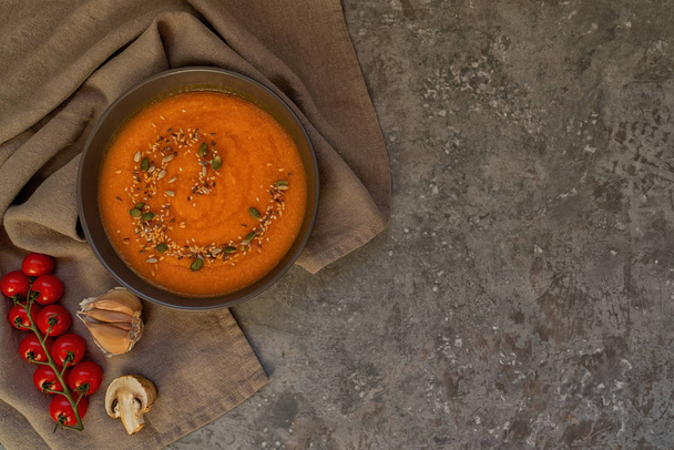 Traditional fall dishes, hot and spicy pumpkin soup with pumpkin seeds and cream on gray stone table. Autumn dinner. Organic vegetables and healthy food concept. Top view with copy space. Toned image - Photo, image