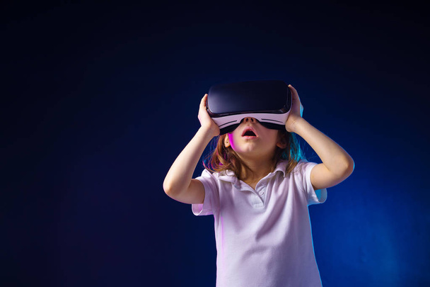 Girl 7 y.o. experiencing VR headset game on colorful background. Surprised emotions on her face.Child using a gaming gadget for virtual reality. - 写真・画像