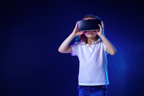 Chica 7 y.o. experimentar juego de auriculares VR en un fondo colorido. Niño usando un gadget de juego para la realidad virtual
. - Foto, imagen