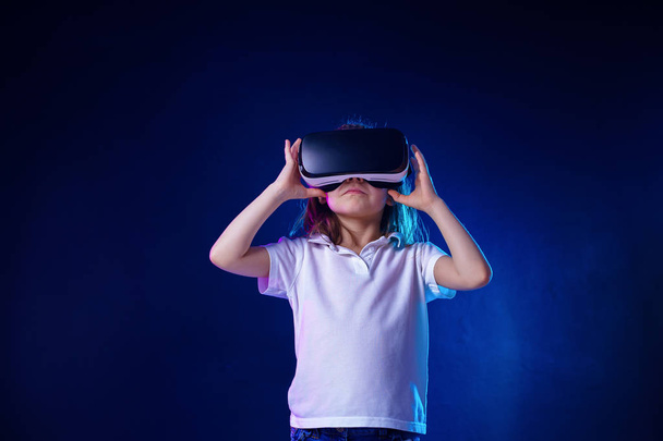 Girl 7 y.o. experiencing VR headset game on colorful background. Child using a gaming gadget for virtual reality. - Φωτογραφία, εικόνα
