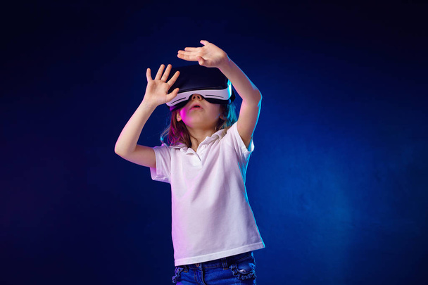 Girl 7 y.o. experiencing VR headset game on colorful background. Child using a gaming gadget for virtual reality. - Foto, Imagem