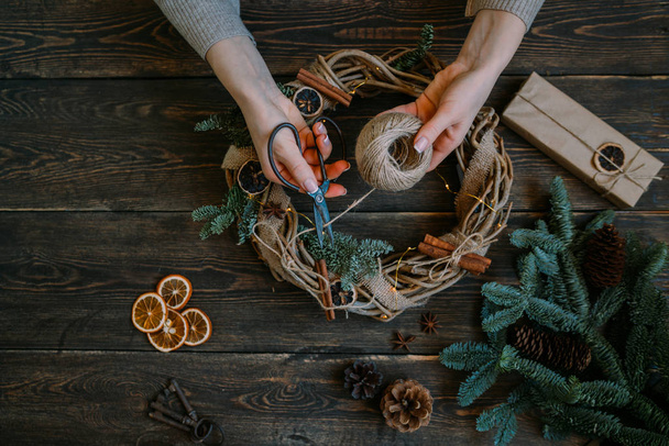 Christmas background with decorations, garland and pine cones. Creating wreath made of christmas tree branches and dry spice on dark vintage wooden board. Happy New Year. Toned image. Soft focus. - Foto, imagen