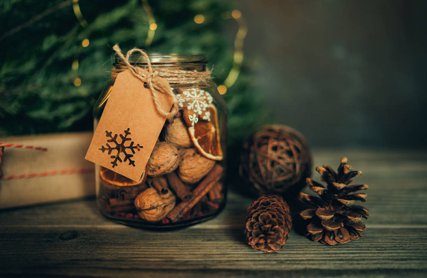 Christmas gift with homemade gingerbread cookies, nuts and chocolates. Glass jar, fir branches, Christmas spices and decor. Winter holidays, New Year or Christmas concept. Toned image. Soft focus. - 写真・画像