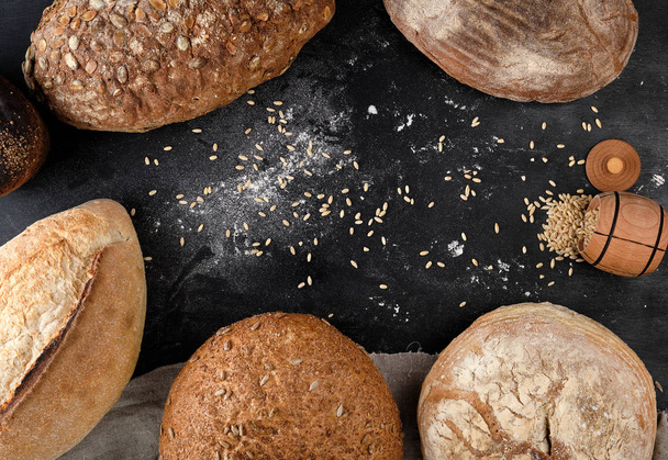 baked different loaves of bread on a black background - Foto, Bild
