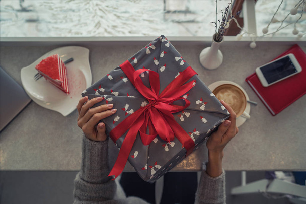 Close up shot of female hands holding a big gift wrapped with red ribbon. Big gift in the hands of a woman indoor. Shallow depth of field with focus on the big box. - Фото, изображение