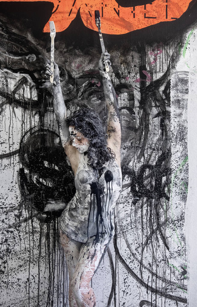 vrouwelijke kunstenaar geschilderd in zwart-wit verf, staande voor een ontworpen muur in de Studio - Foto, afbeelding