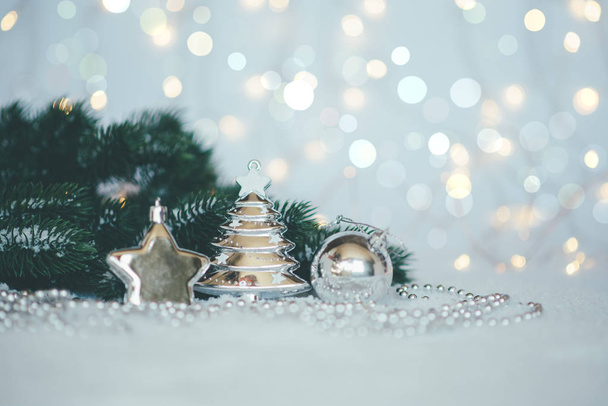 Christmas background with a silver decorations and fir in snow on the blurred, sparkling background. Toned image with copy space. Selective focus. - Photo, Image