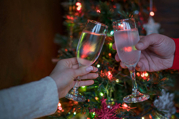 Kaksi lasillista samppanjaa nostettiin maljassa joulukuusen hohtavia valoja vasten. Loma ja yhdessä perheen joulua ja onnellista uutta vuotta. Juhlien aika. Pari samppanjan kanssa. Valikoiva painopiste
. - Valokuva, kuva