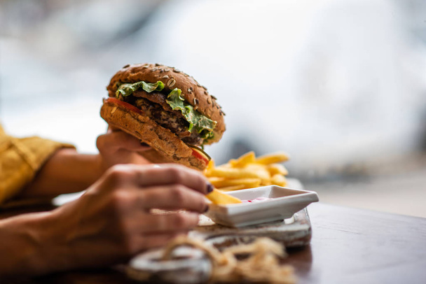 Young girl holding fast food burger, american meal. Tasty grilled made burger with beef, tomato, cheese, cucumber and lettuce. Mockup space for text message or design. - Photo, Image