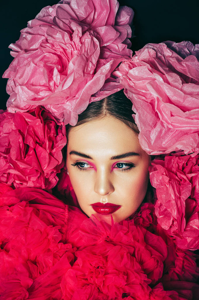 Close up portrait of beautiful young model with bright fashion makeup, wearing big pink fluffy collar, covered with decorative paper flowers - Zdjęcie, obraz