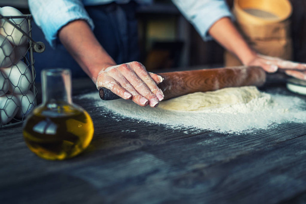 Female hands making dough in ball shape. Basic homemade dough with ingredients on the side on wooden table with natural light. Home healthy food. Selective focus. Focus on the dough. - Foto, Imagem