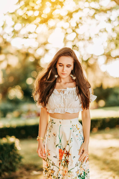Outdoor summer portrait of young beautiful girl with shiny long hair, wearing white blouse and colorful skirt - Φωτογραφία, εικόνα