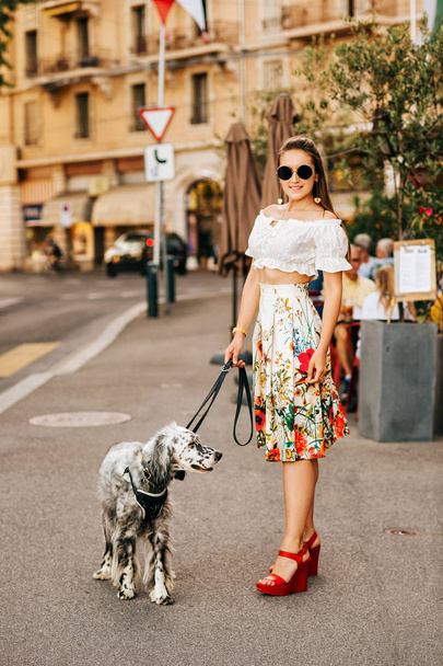 Beautiful young woman walking down the street with dotted white pointer purpurebred dog - Fotó, kép