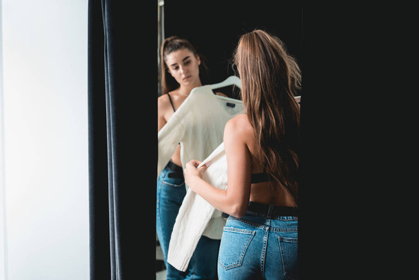 молодая красивая женщина делает покупки, в примерочной в торговом центре моды, примеряет белый свитер
 - Фото, изображение