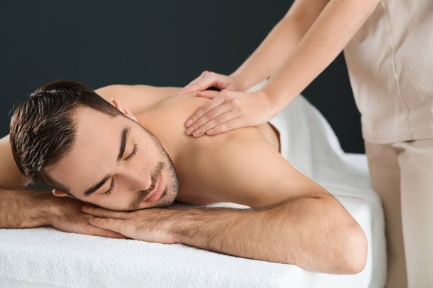 Handsome man receiving back massage on black background. Spa service - Фото, изображение