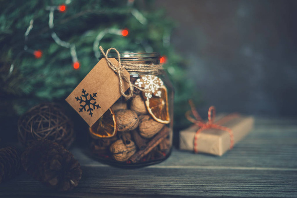 Christmas gift with homemade gingerbread cookies, nuts and chocolates. Glass jar, fir branches, Christmas spices and decor. Winter holidays, New Year or Christmas concept. Toned image. Soft focus. - Foto, Imagem