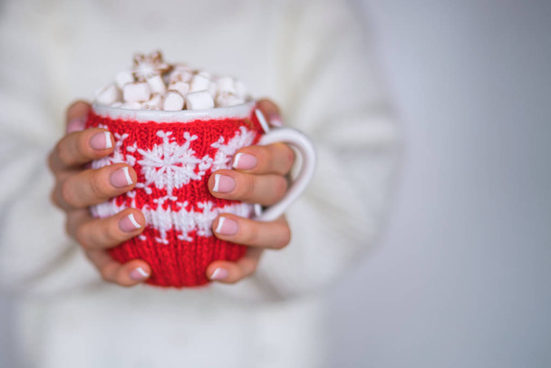 Woman wearing in a white warm sweater, drinking hot tea or coffee from festive cup. Christmas Holidays. Hot drinks and people concept. Toned image. Selective focus. - Foto, Imagen