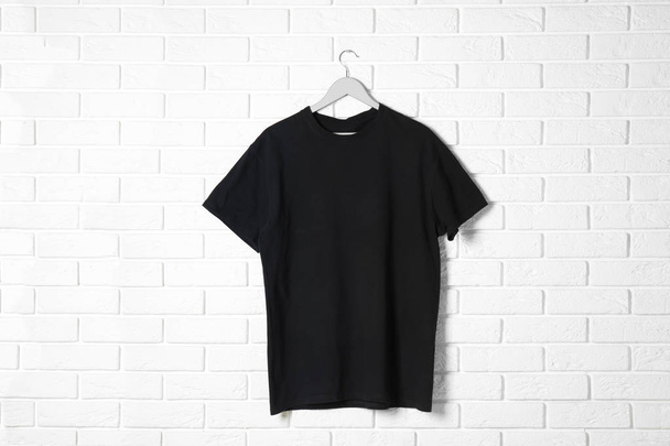Hanger with black t-shirt against brick wall. Mockup for design - Zdjęcie, obraz