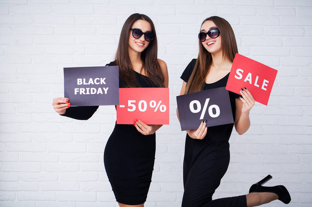 Shopping. Two women holding black bags on light background in black friday holiday - Photo, Image