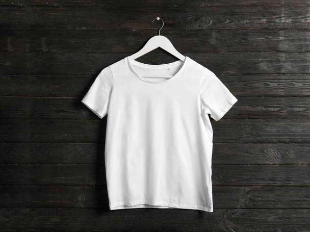 Hanger with white t-shirt on wooden background. Mockup for design - Фото, изображение