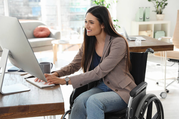 Young woman in wheelchair using computer at workplace - 写真・画像