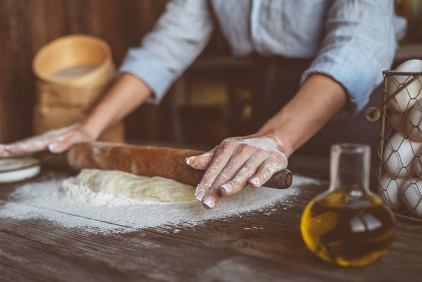Homemade raw pastry on a wooden table on a rustic wooden surface with a rolling pin, flour, butter, wheat spikelets. - Foto, Bild