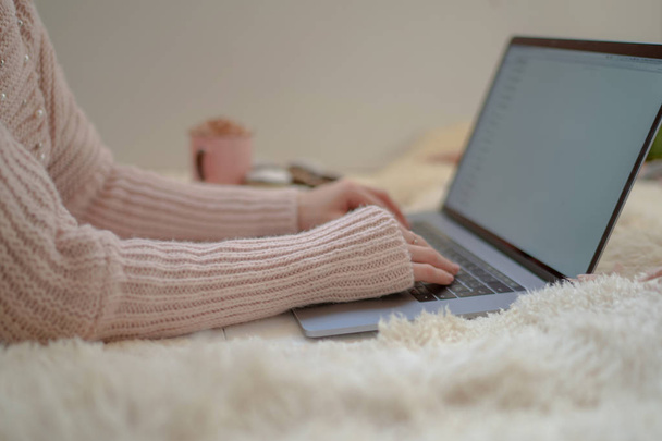 Soft cozy image. Girl in warm sweater lying on floor near cup of coffee and cookies. Side view of a girl' hands. Woman drinking coffee in early morning and reading emails on laptop. Christmas eve. - Foto, afbeelding