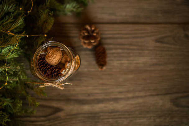 Christmas gift, spices and decor in the glass jar, pine cones, fir branches on wooden brown background. Copy space for your text. Holidays, winter, Christmas presents concept. Toned image. Soft focus. - Фото, зображення