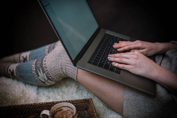 Christmas online shopping. Woman buys presents, prepare to xmas eve. Female with laptop, copy space on screen. Hot coffee, spice and almond cakes on tray. Cozy blanket. Toned image. Soft focus. - 写真・画像