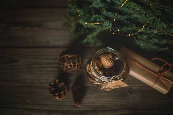 Christmas gift, spices and decor in the glass jar, pine cones, fir branches on wooden brown background. Copy space for your text. Holidays, winter, Christmas presents concept. Toned image. Soft focus. - Photo, image