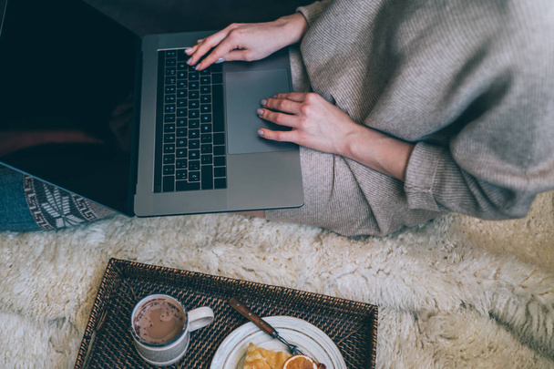 Christmas online shopping. Woman buys presents, prepare to xmas eve. Female with laptop, copy space on screen. Hot coffee, spice and almond cakes on tray. Cozy blanket. Toned image. Soft focus. - Photo, Image