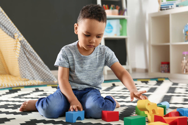 Cute little African-American child playing with building blocks on floor in kindergarten. Indoor activity - Fotoğraf, Görsel