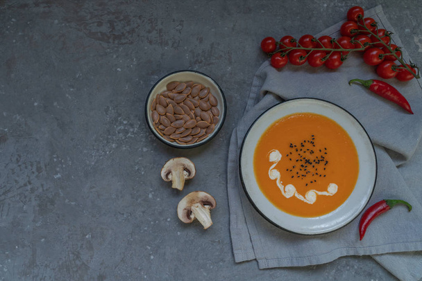 Seasonal autumn food. Spicy pumpkin ans carrot soup with cream and seasoning in rustic bowl on dark gray background. Hot, fresh vegetable soup. View from above with copy space. Toned image. - Photo, image