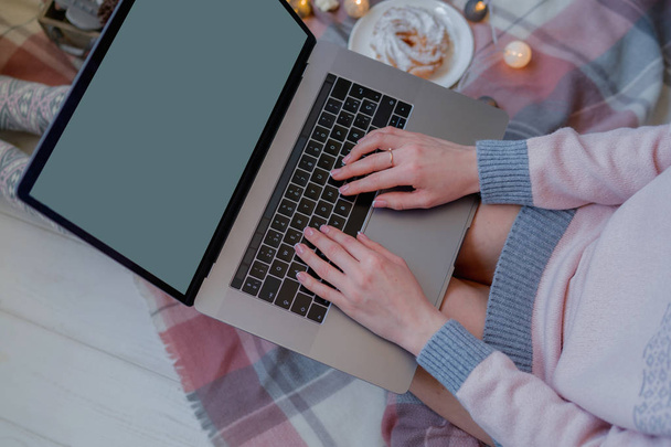 Thuis genieten van Kerstmis. Jonge vrouw werken aan laptop en koffie drinken terwijl zittend op een vloer thuis. Top View mockup afbeelding van meisje gebruik en typen op laptop met blanco wit scherm. - Foto, afbeelding