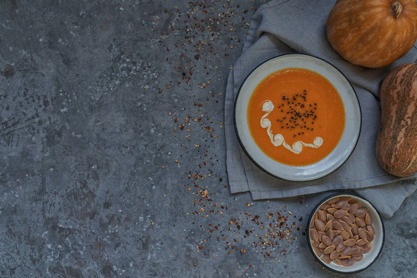 Traditional fall dishes, hot and spicy pumpkin soup with pumpkin seeds and cream on gray stone table. Autumn dinner. Organic vegetables and healthy food concept. Top view with copy space. Toned image - Photo, image