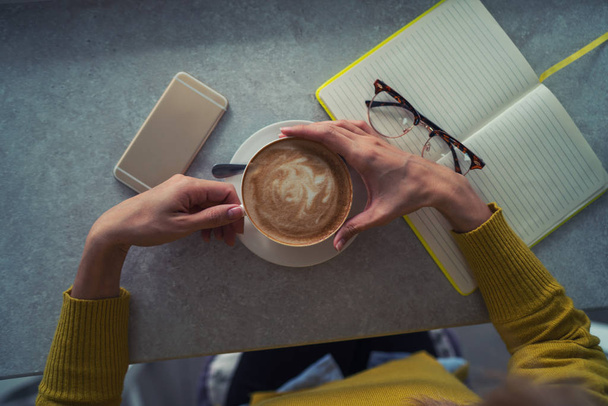 Female hands holding cup of coffee on table background. Coffee cup in coffee shop. Closeup image woman drinking hot coffee in cafe. Vintage style effect picture. Selective focus. - Φωτογραφία, εικόνα