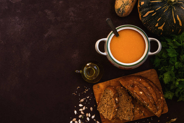 Bowl of pumpkin organic soup with cream and pumpkin seeds on gray background. Dietary vegetarian food. Concept of healthy eating food. Homemade autumn soup. Top view with copy space. Toned image. - Foto, imagen