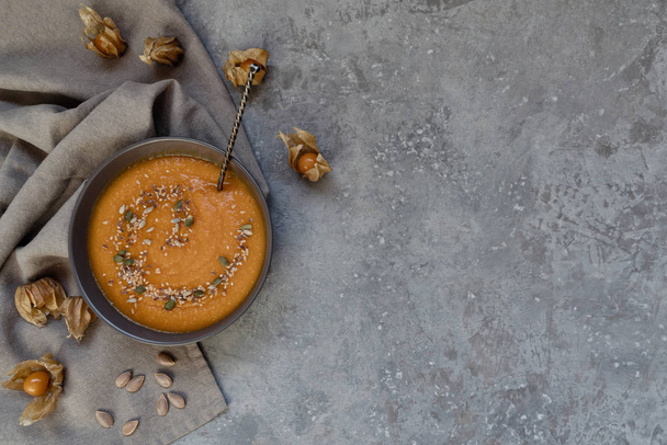 Traditional fall dishes, hot and spicy pumpkin soup with pumpkin seeds and cream on gray stone table. Autumn dinner. Organic vegetables and healthy food concept. Top view with copy space. Toned image - Photo, Image