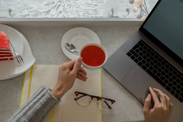 Empreendedor com um laptop relaxante em uma cafeteria desfrutando de uma xícara de chá de frutas. Xícara de chá quente em um fundo de janela de inverno gelado. Ambiente aconchegante café no inverno. Foco seletivo
. - Foto, Imagem