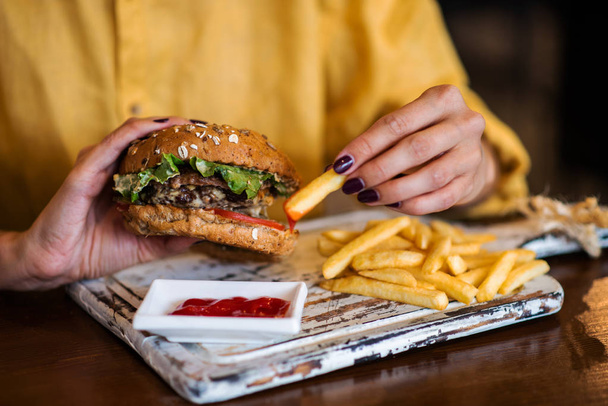 Tasty grilled made burger with beef, tomato, cheese, cucumber and lettuce. Woman holds burger in hands. - Foto, Imagen