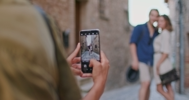kobieta fotografowanie zdjęcie ze smartfonem do szczęśliwych przyjaciół turystycznych ludzi w małej ulicy odwiedzając wiejskie miasto Spello.Back follow.Friends włoski podróż w Umbria.4k zwolnionym tempie - Materiał filmowy, wideo