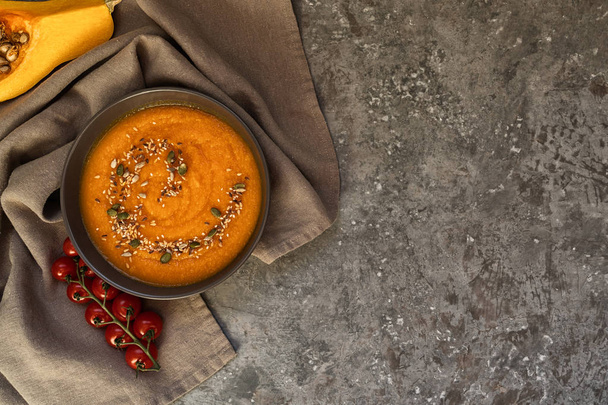 Bowl of pumpkin organic soup with cream and pumpkin seeds on gray background. Dietary vegetarian food. Concept of healthy eating food. Homemade autumn soup. Top view with copy space. Toned image. - Valokuva, kuva