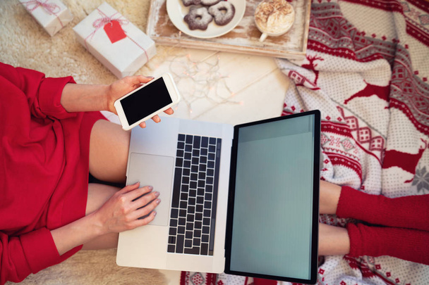 Akıllı telefondan mesaj okuyan genç bir kadın evinde dizüstü bilgisayarla oturuyor. Çevrimiçi satın almak için ücretsiz internet bağlantısı yoluyla cep telefonuna yeni uygulama yükleniyor. - Fotoğraf, Görsel