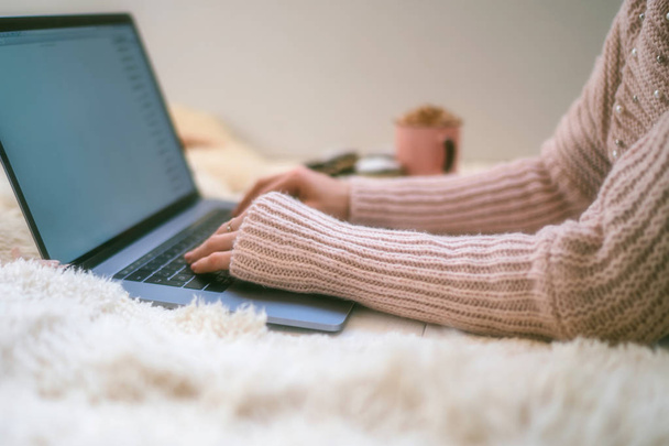 Soft cozy image. Girl in warm sweater lying on floor near cup of coffee and cookies. Side view of a girl' hands. Woman drinking coffee in early morning and reading emails on laptop. Christmas eve. - Foto, Imagem